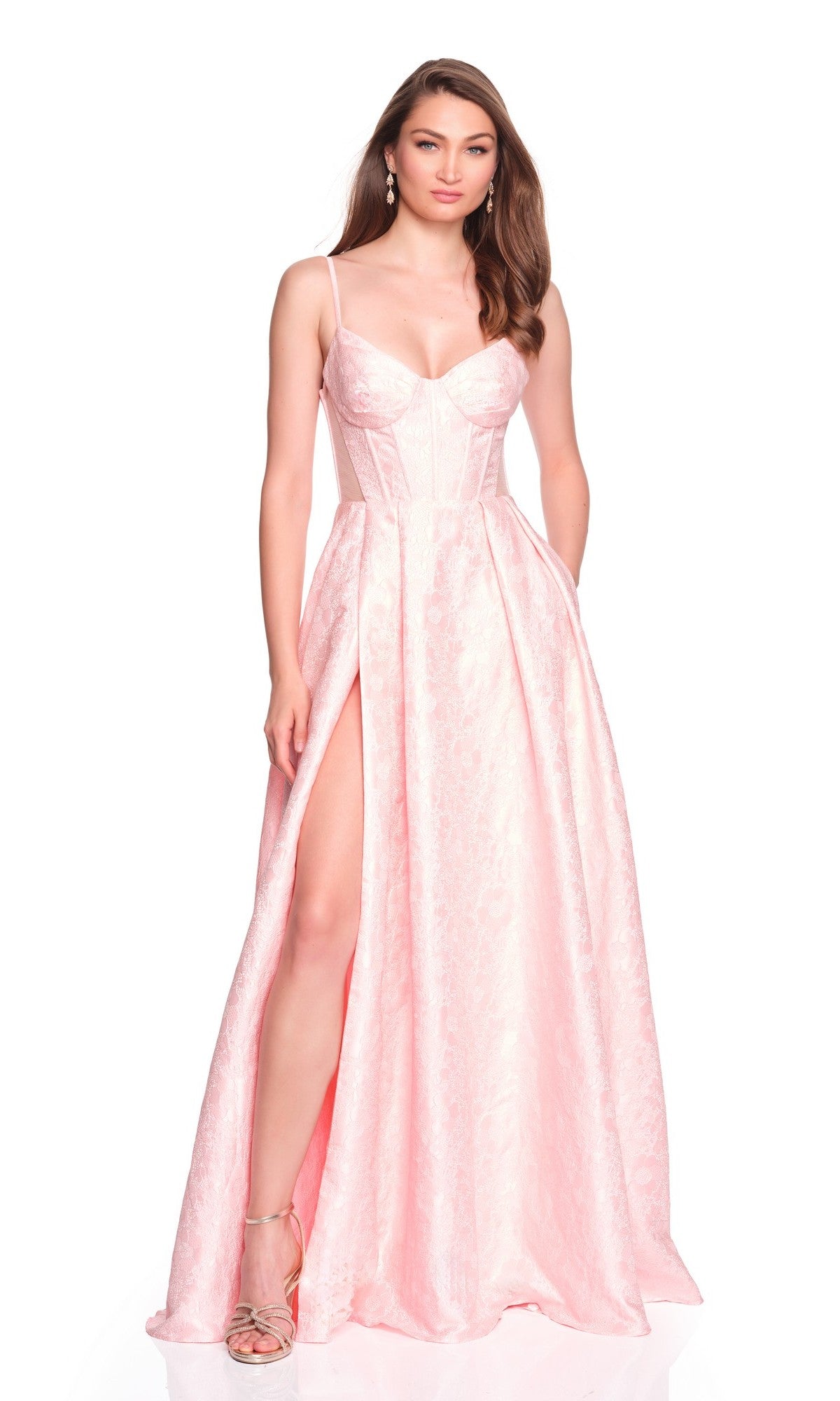 A woman wears the Dave and Johnny 12885 long prom dress in light pink, featuring thin straps, a corset bodice, and a high-leg slit, standing against a white background.
